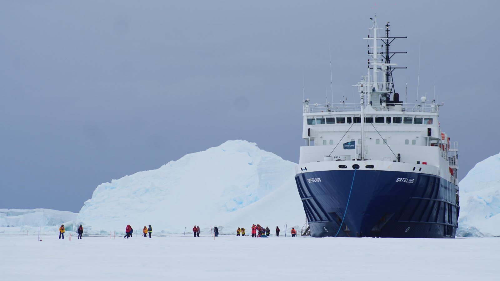Die MS Ortelius liegt im antarktischen Meereis, davor Gäste auf der Eisfläche