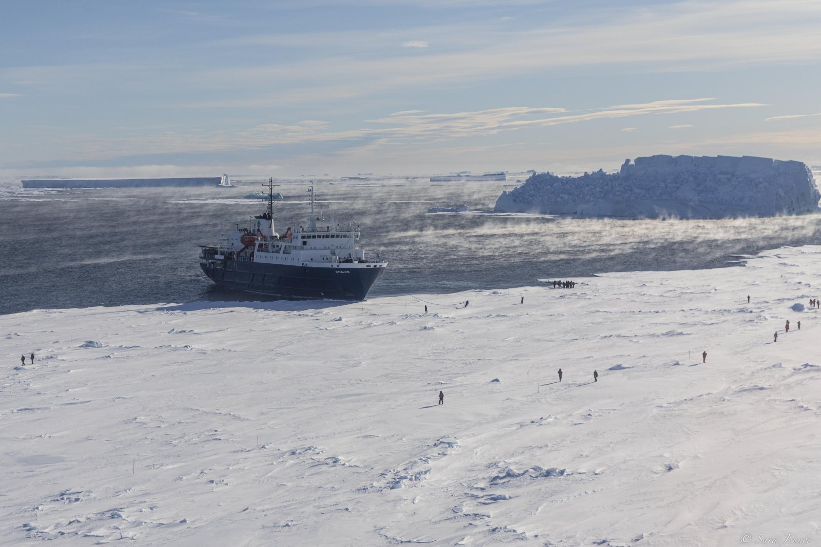 Expeditionsschiff im Packeis, davor eine weite Eisfläche mit einzelnen Menschen