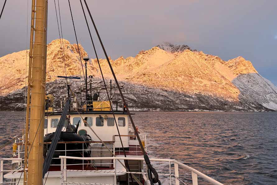 Blick über das Vordeck der MS Cape Race auf verschneite Berge, deren Gipfel im Morgenlicht golden leuchten