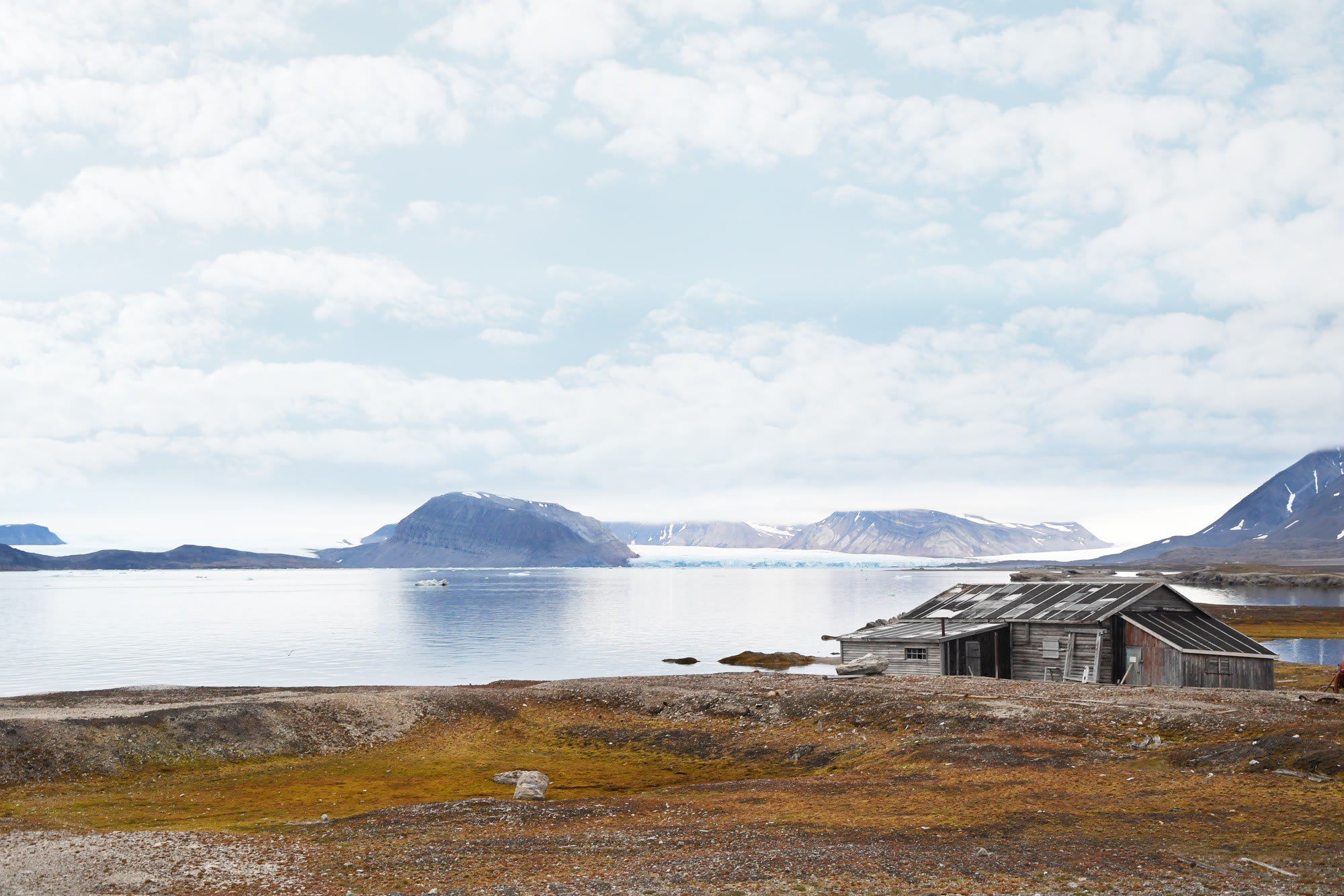 Alte hölzerne Trapperhütte an der Küste Spitzbergens vor Fjord und Bergen