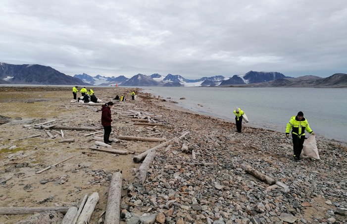 Gäste sammeln bei einer Strandreinigung an einem weiten Kiesstrand in Spitzbergen angeschwemmten Müll