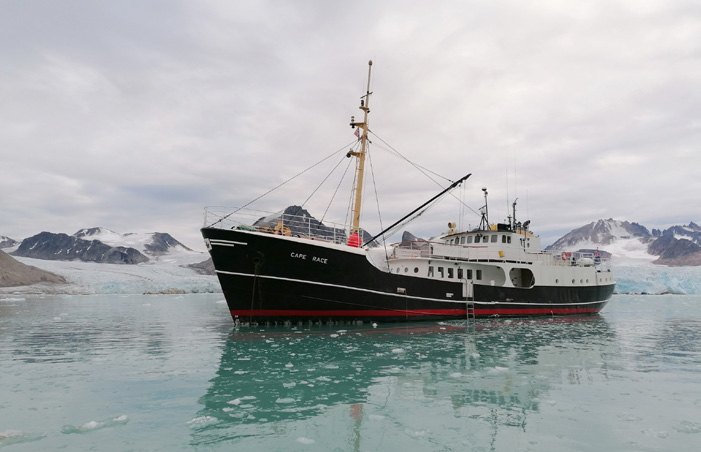 Kleines Expeditionsschiff in türkisfarbenem Wasser vor schneebedeckten Bergen in Spitzbergen